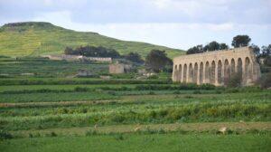 Gozo aqueduct seen from a distance with green fields and hills behind and all around