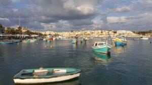 Blue and yellow boats floating on the sea surface at a rural area with clouds in the sky. The sun is peeking through