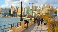 Sliema's Promenade on a sunny day, with a view of the cityscape and a corner of the sea.