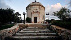 Small decadent tan colored chapel perched on a stone platform atop a short stone staircase.