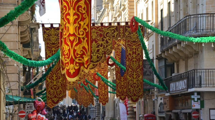 Traditional Maltese red and yellow banners with green and red garlands attached, hanging above a busy street in Valletta.