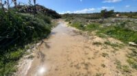 A flooded pathway with hills and grass on the side