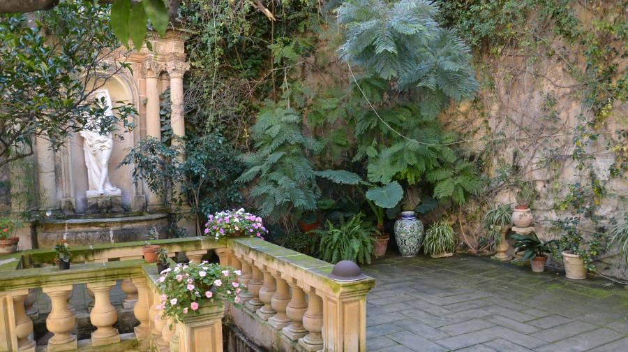 An interior garden court in Casa Rocca Piccola. A fountain with a statue at one side, greenery spilling over the walls and a decadent staircase descending out of view.