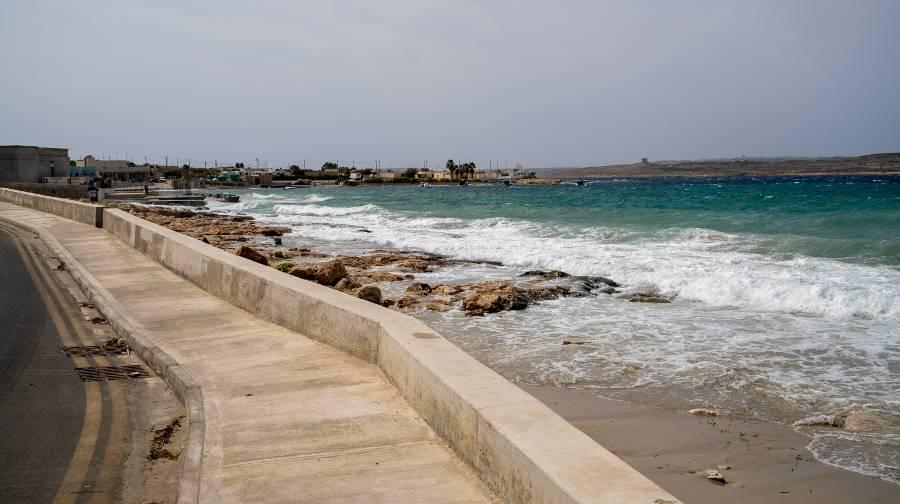 An ivory colored sidewalk and road with a view of a Mellieha rocky beach with grey skies.