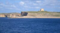 A foreground of sea and background of an island with a white tower on top