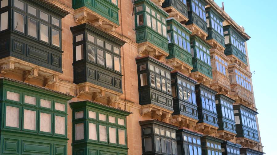 A limestone tan coloured building with a grid of Maltese Gallarija balconies, mostly in a dark green, forrest green and tan colour.