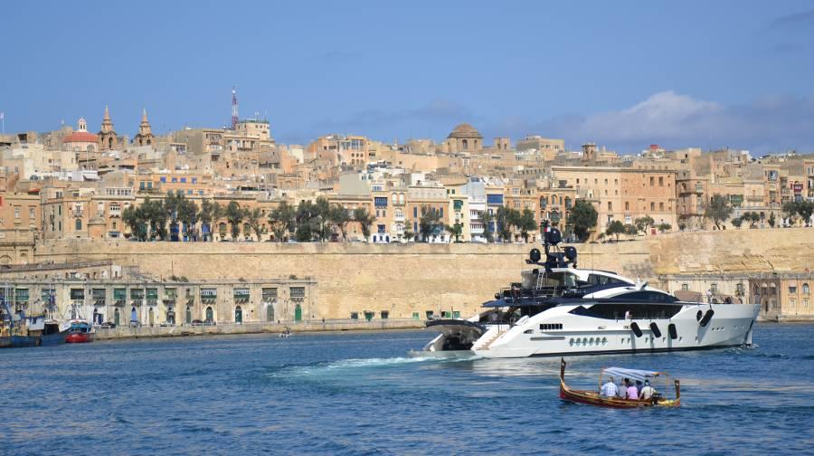 Valetta seen from accross the harbour and a small boat sailing towards it. A yacht sails the other direction.