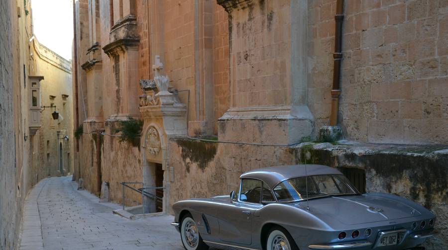 Narrow street in Mdina during daytime with a grey car parked at the side.