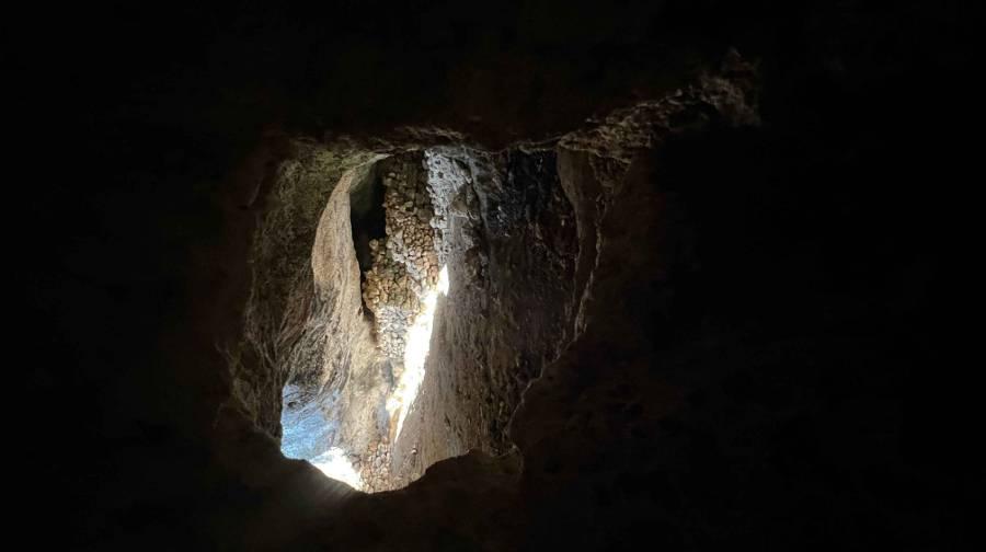 A dark image with an opening in the middle into an open area of a cave